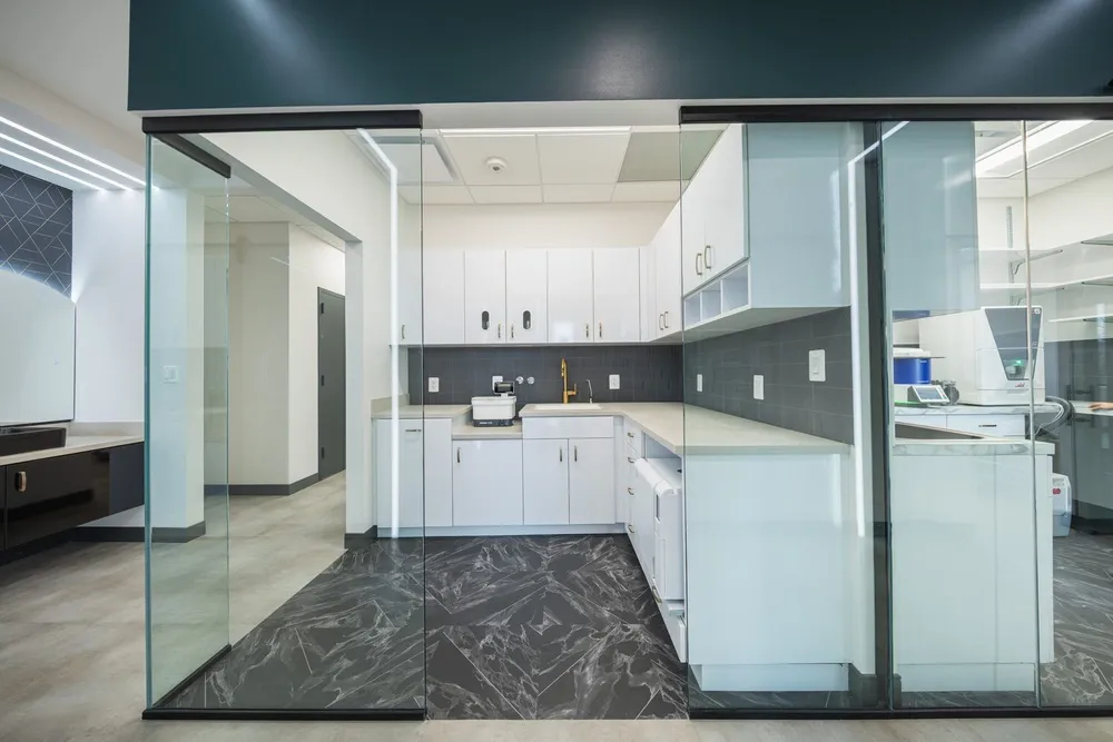 View into the sterilization lab through a glass partition: white cabinetry, dark backsplash, polished tile.