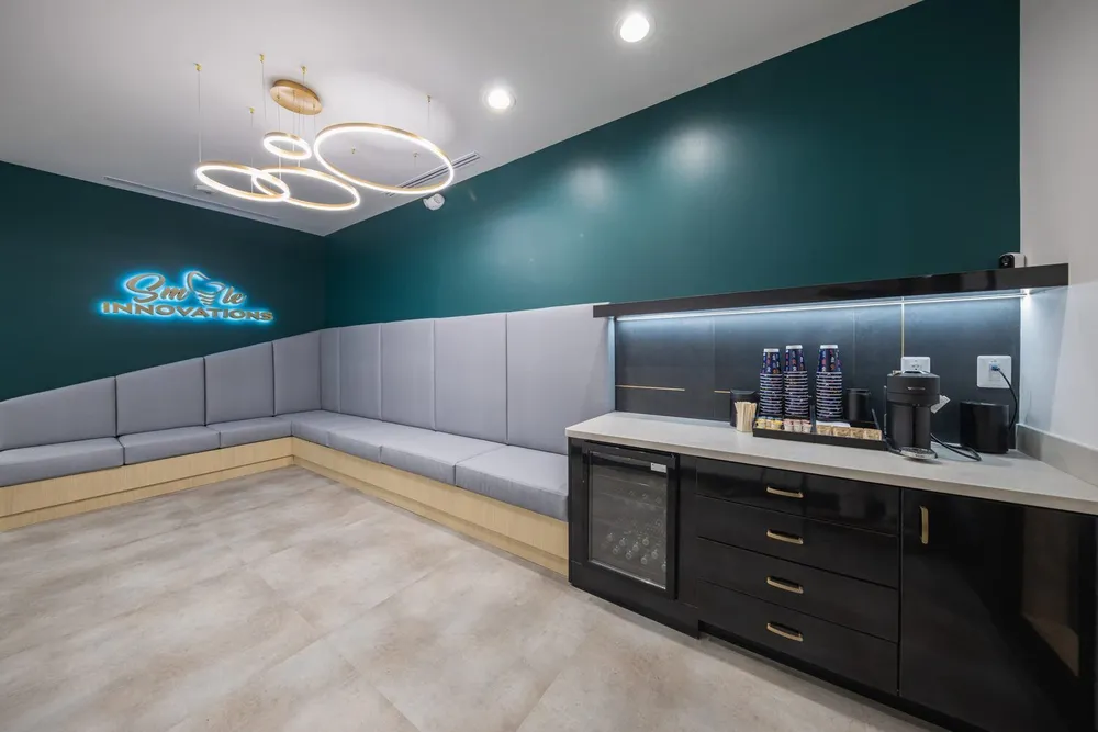The waiting area: long upholstered bench, backlit Smile Innovations signage on the deep teal accent wall, brass pendant lights.