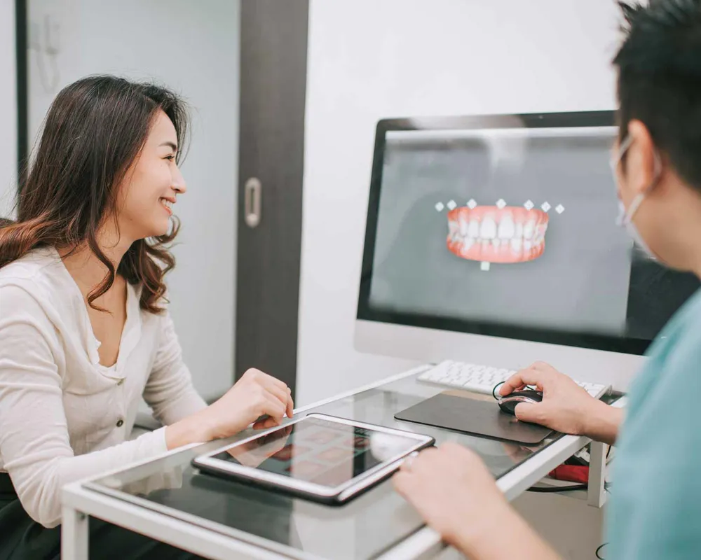 A patient and clinician reviewing a 3D digital model of the patient's teeth on a chairside monitor.